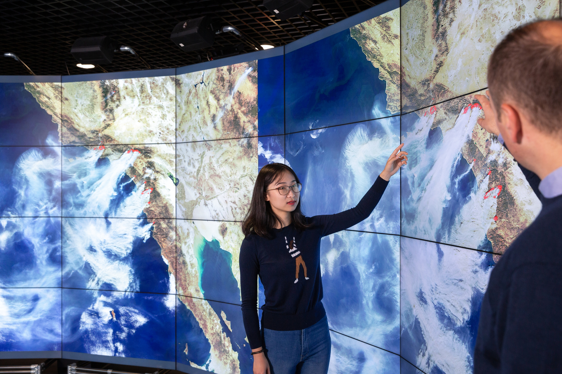 People pointing to large screen showing weather systems
