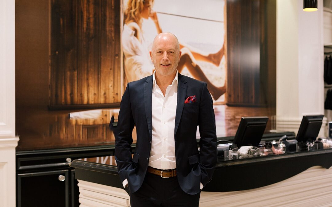 A professional man in a dark suit and white shirt stands in a modern office space, representing entrepreneurial mentorship and business leadership.
